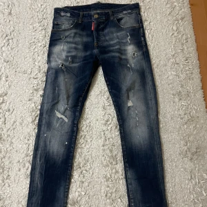 Dsquared2 blå slitna jeans, stl 50 - Snygga blå jeans från Dsquared2 med slitna detaljer och distressed look. Klassisk femficksmodell med smal passform och tydliga slitningar framtill och baktill. Jeansen har Dsquared2-logga på röd etikett och är tillverkade i bomull.