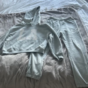 Ett turkost/grönt mjukis sett från Lager 157  - Säljer ett mjukissett i turkos/grönt. Det är ett par mjukisbyxor från Lager 157 i storlek XS som har resår i midjan och vid bensluten för en skön och avslappnad passform. Hoodien är i Storlek Xs/S med knyte i luvan och resår vid magen samt slutet på ärmarna. Perfekta för de mer lugna dagar eller när du vill vara extra bekväm. Materialet är mjukt och värmer gott. Endast använt några gånger och texten är lite rivig när man trycker ut den på magen (LA). Köptes för 399. 