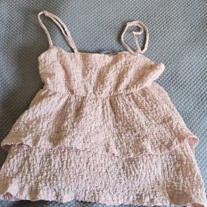 volangtop - Supersöt ljusrosa volang topp från Gina Tricot med smala axelband och volangig, rynkad struktur. Toppen har en luftig och flowy passform, perfekt för varma dagar. Materialet känns mjukt och lätt mot huden. Toppen är skön och snygg!! Skriv om du är intresserad eller har några frågor! Pris kan diskuteras!🌸