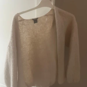 Beige stickad kofta från Bik Bok - Mysig och luftig beige stickad kofta från Lindex Koftan är öppen framtill, har lång ärm och är tillverkad i ett fluffigt, lätt material som känns superbekvämt. 