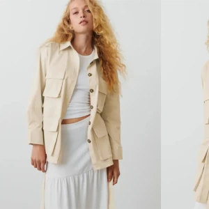 Beige overshirt med bälte och fickor - Stilren beige overshirt med knappar framtill, stora bröst- och sidfickor samt bälte i midjan. Jackan har klassisk krage och långa ärmar med knapp vid ärmslut. Perfekt för lager-på-lager och enkel att styla till olika looks.