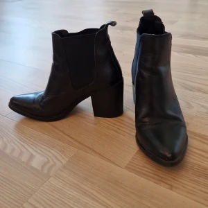 Steve Madden Svarta chelsea boots med klack - Snygga svarta Steve Madden chelsea boots i skinn med markerad klack och spetsig tå. Klassisk elastisk resår på sidorna och dragflik bak för enkel påtagning. Perfekta för dig som vill ha en stilren och edgy look till höst och vinter.