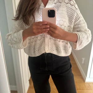 Vit stickad kofta från Indiska - Säljer en vit, stickad kofta från Indiska i storlek XS. Koftan är croppad med långärmad passform och har ett snyggt hålmönster samt knappar framtill.