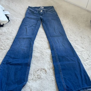 Blå bootcut jeans från Nelly - Snygga blå jeans från Nelly med bootcut passform och låg midja. Jeansen har dubbla knappar i midjan och coola broderade detaljer på bakfickorna. Perfekta för dig som gillar en klassisk men trendig look.