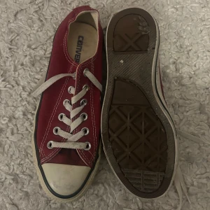 Röda Converse sneakers, storlek 38 - Säljer ett par klassiska röda Converse sneakers med vit tå och vita snören. Skorna har rund tå, platt sula och är tillverkade i slitstark bomullstextil. Perfekt för dig som gillar retrostil och vill ha ett par ikoniska sneakers i garderoben.