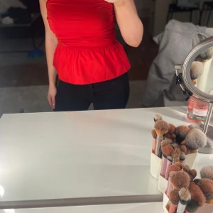 Röd bandeau topp med volang - Snygg röd bandeau topp med volang nertill och smockad midja. Toppen är axelbandslös men bärs här med svarta axelband. Perfekt för dig som vill sticka ut med en färgstark look och markerad midja.