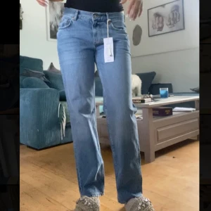 Lågmidjade raka jeans i mellanblå denim - Säljer ett par snygga lågmidjade raka jeans från Gina Tricot i mellanblå tvätt. Modellen är petite och har klassisk femficksdesign, bälteshällor och dragkedjegylf. Perfekta för en avslappnad och trendig look, aldrig använd med prislapp på.