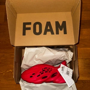Adidas Yeezy Foam RNNR ”Vermillion” - Säljer ett par Adidas Yeezy Foam Runner i helrött. Skorna har futuristisk design med många hål och är tillverkade i lätt syntetmaterial. Perfekta för dig som vill sticka ut med något riktigt unikt och bekvämt på fötterna nu i sommar. Storlek eu 42, us 8, uk 8. Helt oanvända, dvs DSWT, och original låda medföljer. Priset är aningen förhandlingsbart. 