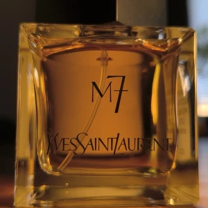 Yves Saint Laurent M7 Eau de Toilette - YSL M7 Eau de Toilette i en stilren, fyrkantig glasflaska med bärnstensfärgad vätska. Doften har noter av mandarin, oud, patchouli, ciste och myrra. Flaskan rymmer 80 ml och har tydlig logga och svart lock. En ikonisk och djup parfym från 2002.