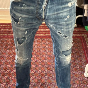 Dsquared2 Jeans Cool guy slim fit - Riktigt snygga blå jeans från Dsquared2 med slitningar och feta detaljer från modellen ”Cool guy”                                                                              strl 44 som motsvarar 28-29. Har lagat baksidan av jeansen men inget som syns utifrån. Därav ett schysst pris. Köpt från luisaviaRoma. 