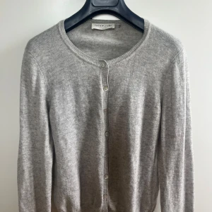 Kashmir kofta - Ljusgrå kofta från Rosemunde i kashmir, nypris 800 kr. Står ingen storlek, men motsvarar en S. Kommer med en extra knapp, se bild. Har lite mörkare färgningar på axlarna, därav priset.