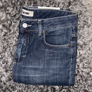 Mörkblå jeans från Acne Studios - Snygga mörkblå jeans från Acne Studios med klassisk femficksdesign och diskret tvätt. Jeansen har raka ben och normal passform, med tydliga kontrastsömmar och vit logopatch bak i midjan. Perfekta för en stilren och avslappnad look.