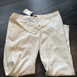 Vita kostymbyxor från BikBok med prislappen kvar - Snygga vita kostymbyxor från BikBok i storlek 42. Byxorna har klassisk passform med hällor för bälte och stängs med dragkedja och hake. Perfekta för en clean och stilren look.