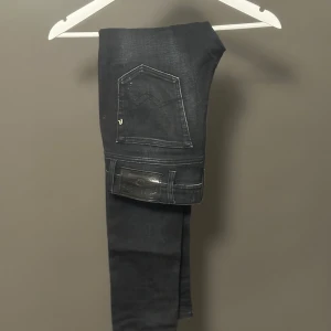 Replay Jondrill svarta Slim jeans - Säljer ett par svarta Replay Jondrill jeans i Slim fit. Jeansen har fem fickor, snygga slitningar och klassisk Replay-logga på bakfickan. De är tillverkade i stretchigt jeanstyg för en tight och bekväm passform.