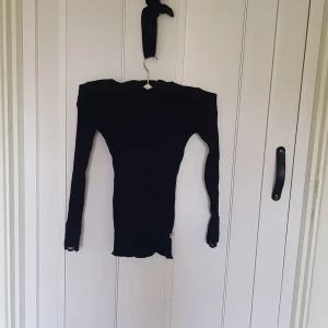 Svart ribbad tröja med spets POMPdeLUX - Svart långärmad tröja från POMPdeLUX i ribbad bomull med snygga spetsdetaljer vid ärmsluten. Tight passform som sitter snyggt och ger en stilren look. Perfekt att matcha med jeans eller kjol för en trendig outfit.