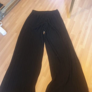 Svarta ribbade byxor från KappAhl - Svarta vida byxor från KappAhl med ribbad struktur. Byxorna har resår i midjan och är tillverkade i ett mjukt material som ger en skön och avslappnad känsla. Perfekta för en chill look och passar till sneakers eller chunky boots.