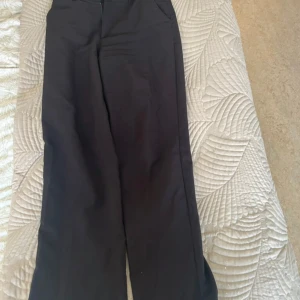 Kostymbyxor - Svarta kostymbyxor från Madlady i storlek 38. Byxorna har en klassisk wide fit med hög midja och bälteshällor. Slitage på ena insida lår som visas på en av bilderna. 