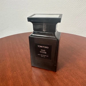 Tom Ford Oud Wood 100ml EdP - Tom Ford Oud Wood Eau de Parfum i en lyxig, mörkgrå glasflaska på 100 ml. Flaskan har en stilren, fyrkantig design med svart etikett och silverdetaljer på locket. En ikonisk doft med exklusiv känsla och elegant utseende.