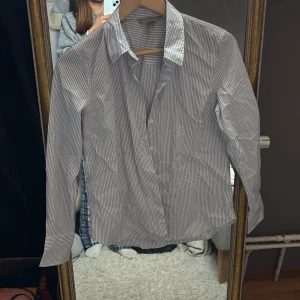 Randig skjorta i bomull - Snygg skjorta med smala blå och vita ränder. Klassisk krage, långärmad och knäppning framtill. Perfekt till jeans eller kostymbyxor för en clean och stilren look. Tillverkad i mjuk bomull som känns skön mot huden.