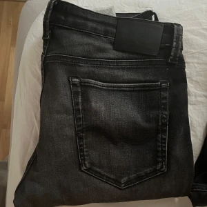 Svarta slim jeans från Jack & Jones - Svarta slim fit jeans från Jack & Jones med superstretch för extra komfort. Jeansen har klassisk femficksdesign, svarta sömmar och en snygg tvättad look. Perfekta för dig som gillar en smalare passform och stilren vibe.