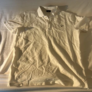 Vit pikétröja från GANT - Klassisk vit pikétröja från GANT med korta ärmar och krage. Tröjan har knappar framtill och en liten broderad logga på bröstet. Tillverkad i mjuk bomull som känns skön mot huden. Perfekt för en clean och stilren look.