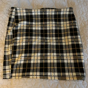 Rutig kortkjol från FB Sister, stl L - Superfin kortkjol från FB Sister i storlek L. Kjolen har ett rutigt mönster i svart, vitt och gult och är figurnära med klassisk rak passform. Perfekt för dig som gillar preppy vibes och vill sticka ut lite extra.