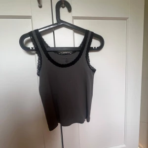 Topp från Brandy Melville - Supersöt grå linnetopp från Brandy Melville med svarta spetsdetaljer längs urringning och axelband. Säljer då den inte kommer till användning 💓