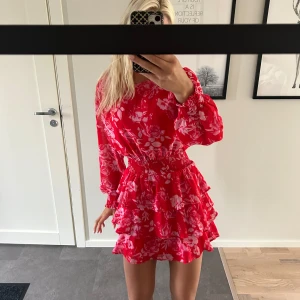 Röd blommig volangklänning från Gina Tricot - Superfin röd kortklänning från Gina Tricot med rosa blommigt mönster, långa ärmar och smock i midjan. Bra skick och storlek 40 men skulle säga att den passar s/m.