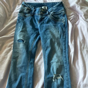 Blå slitna jeans från LTB - Snygga blå jeans från LTB med slitningar och hål på benen för en trendig look. Klassisk femficksmodell med kontrastsömmar och knäppning med tre knappar. Perfekta för dig som gillar en avslappnad och cool stil.