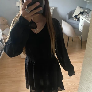 Svart kortklänning med v-ringning - Supersnygg svart kortklänning med v-ringning och långa ärmar. Klänningen har en lätt volang nertill och markerad midja som ger en fin siluett. Perfekt för dig som gillar en stilren look med lite extra flärd. Oanvänd, pris går att diskuteras💞