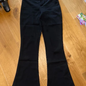 Svarta bootcut-byxor Gina Tricot XS - Svarta kostymbyxor från Gina Tricot i storlek XS. Byxorna har utsvängda ben, två bakfickor med knappar och är tillverkade i ett mjukt tyg som känns bekvämt. Perfekta för dig som gillar en klassisk och stilren look. 