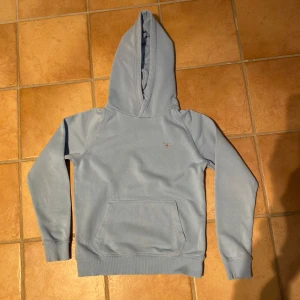 Ljusblå hoodie från Gant - Snygg ljusblå hoodie från Teen Gant med klassisk känguruficka och liten broderad logga på bröstet. Tröjan har huva och långa ärmar med ribbade muddar. Perfekt för en chill och avslappnad stil. Den är väldigt skön och lagom tjock! Ca. 1000 kr nypris.