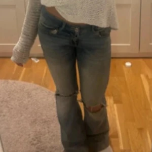 Lågmidjade bootcut jeans med slitning - Säljer ett par ljusblå jeans med låg midja och bootcut-modell. Jeansen har slitningar och hål vid knäna för en trendig look. Klassisk femficksdesign och tillverkade i denim. Perfekta för dig som gillar en avslappnad och cool stil.