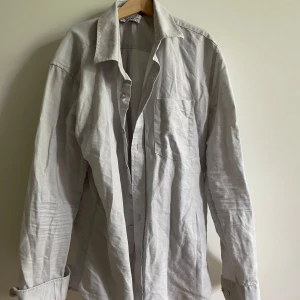 Ljusgrå linneskjorta i bomull - En ljusgrå skjorta ifrån Ahlqvist Clothing. Säljer skjortan då jag växt ut den och har ingen användning för den längre. Skjortan är i topp skick och har inga skador. 