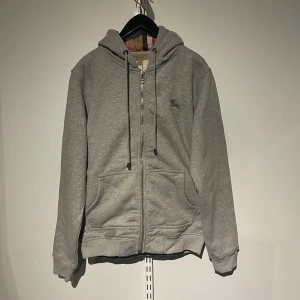 Grå burberry hoodie - Säljer en grå Burberry hoodie då den är för liten. Jag har haft den i ca ett halvår, men den är fortfarande i mycket bra skick. Den är storlek M som ni kan se på andra bilden. Om ni har några frågor är det bara att ni hör av er🙌 Kvitto finns!