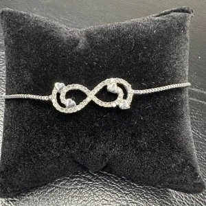 Vintagearmband med evighetssymbol i strass och hjärtan - 80-tal - Retro - Från farmors smyckesskrin - Elegant armband från farmors smyckesskrin med gnistrande strass i form av en evighetssymbol dekorerad med små hjärtan. Smidig dragskolås gör att längden enkelt kan justeras för perfekt passform. Perfekt till vardag och fest – en romantisk vintageaccessoar med charm. Justerbar längd.  Prutpolicy: Priset är redan lågt, så jag prutar inte – men jag erbjuder rabatt vid köp av flera saker.  