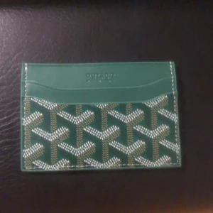 Grön plånbok med mönster - Säljer en grön plånbok med grafiska mönster i vitt och beige. Plånboken har flera kortfack och är tillverkad i skinn med tryckt design. Perfekt för dig som vill ha något stilrent men ändå sticker ut.