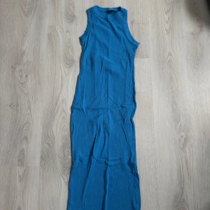 Blå ribbad långklänning - Snygg blå långklänning i ribbat material med ärmlös design och rund halsringning. Perfekt för dig som gillar en enkel men stilren look. Klänningen har en tight passform och är superenkel att styla med sneakers eller sandaler.