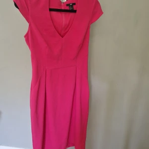 Rosa kortklänning från H&M - Snygg rosa kortklänning från H&M med djup v-ringning och korta ärmar. Klänningen har figurnära passform och dragkedja i ryggen. Perfekt för dig som vill sticka ut med en färgstark look.