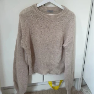 Beige stickad tröja  - Mysig beige stickad tröja med rund halsringning och breda ribbade muddar. Tröjan har en relaxed fit och långa ärmar, perfekt för lager på lager under kyliga dagar. Enkel att matcha med jeans eller kjol för en chill look.