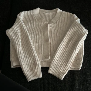 Vit stickad kofta från Kappahl - Säljer en krämvit stickad kofta från Kappahl i storlek 158/164. Koftan har grov ribbstickning, långa ärmar och stängs med tre knappar framtill. Perfekt att slänga på sig när det är lite kyligt ute. Passar bra nu till sena sommarkvällar. 