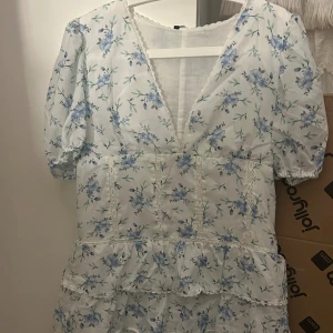 vit volangklänning  - PRISET ÄR DISKUTERBART!!Populär volangklänning med blåa blommor. Storlek L men skulle säga M/L Det är spets detaljer runt om hela klänningen. Finns även en dragkedja på ena sidan. I väldigt bra skick. Köpt här på plick💗