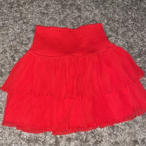 Röd volangkjol från Lindex - Superfin röd kortkjol från Lindex med bred smock i midjan och dubbla volanger. Kjolen har en luftig känsla och är perfekt för dig som gillar färg och volym. Passar dig som vill sticka ut och skapa en lekfull look.