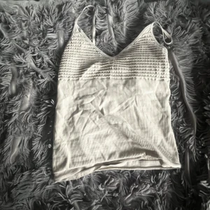 Beige ribbad linnetopp från Choice - Säljer en beige ribbad linnetopp från Choice med smala axelband och v-ringning. Toppen har en smockad överdel och är tillverkad i stretchigt material som sitter snyggt på kroppen. Perfekt för varma dagar eller att styla lager på lager.