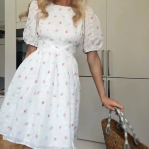 Vit blommig kortklänning - Supersöt vit kortklänning med små rosa blommor, puffärmar och öppen rygg med knyt i nacken. Klänningen har en lätt utsvängd kjol och är gjord i bomullsmix, perfekt för sommarens alla tillfällen🌸☀️ priset går att diskuteras 