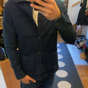 Mörkblå overshirt från John Henric - Snygg mörkblå jeansjacka/overshirt från John Henric i 100% bomull. Klassisk modell med tre stora fickor framtill, knappar hela vägen och krage. Perfekt för dig som gillar stilren och enkel design med en modern touch. Passar S och för en mer sllim fit M (aldrig använd)