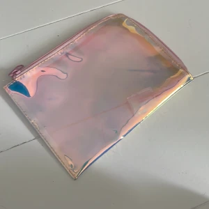 Rosa holografisk necessär  - Säljer en superfin necessär i holografiskt rosa med dragkedja. Väskan har en glansig yta som skiftar i olika färger beroende på ljuset och är perfekt för att förvara småsaker eller smink. 