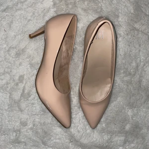 Beige pumps med spetsig tå från XIT - Snygga beige pumps från XIT med spetsig tå och låg klack. Skorna har en glansig finish och klassisk siluett som ger en stilren look. Perfekta för dig som gillar en elegant och tidlös stil.