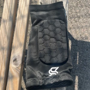 Svart padded sporthandske S - Svart sporthandske från SISU med vadderad hexagonmönstrad ovansida för extra skydd. Tillverkad i stretchigt syntetmaterial som andas. Perfekt för dig som vill ha bra grepp och skydd vid träning eller sport. Snygg och funktionell design med vit logga framtill. Säljer 1 om man behöver 1 till skil sock benskyd 