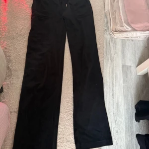 Svarta mjukisbyxor Juicy Couture S - Svarta mjukisbyxor från Juicy Couture i klassisk velour. Byxorna har raka ben, fickor med lock och silverknappar bak samt en bekväm midja. Perfekta för en chill och trendig look.